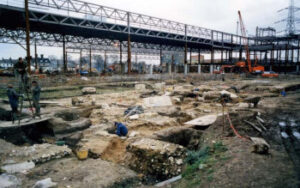 The excavation of the priory church, c.1988, showing the foundations of the church with girders and scaffolding in the background. 